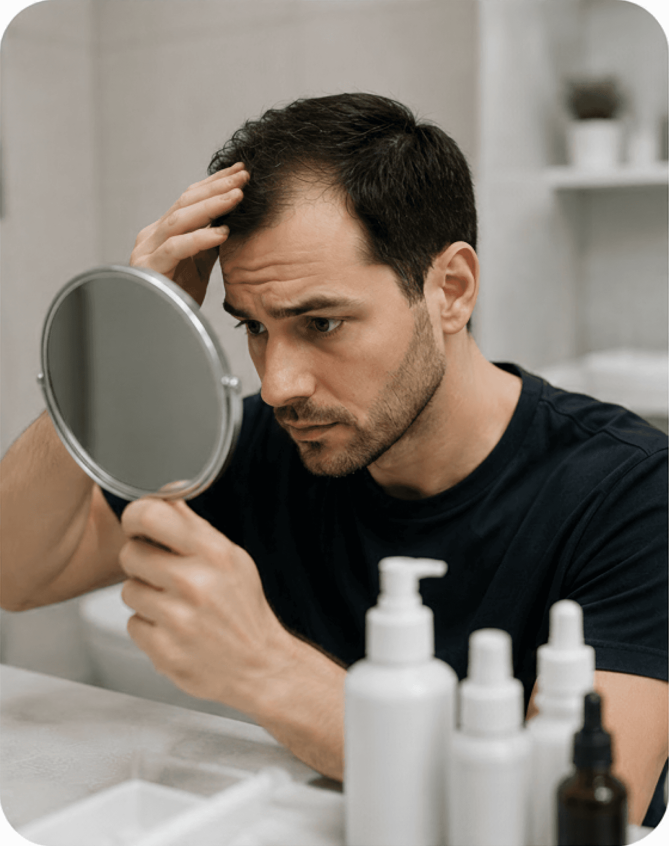 A man checking his hair in a handheld mirror beside treatment products